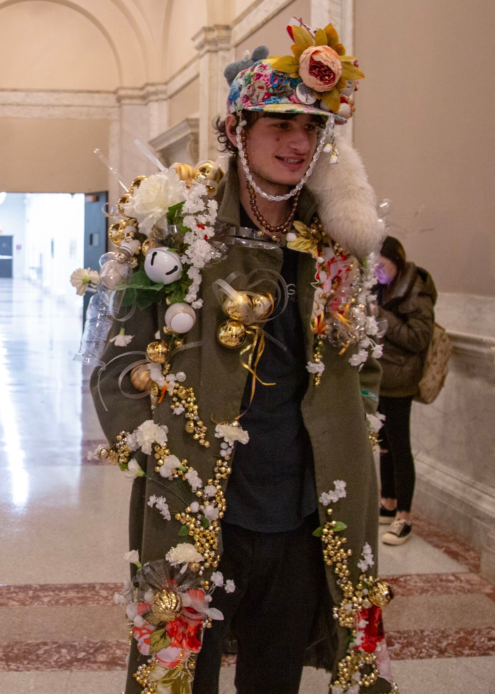 The "Sonitus Strepitus" features ornate embellishments on the shoulders, arranged in a dramatic diagonal perspective to enhance visual impact. The interplay of gold, red, and white hues highlights the military green, adding a distinctive and sophisticated elegance to the ensemble.